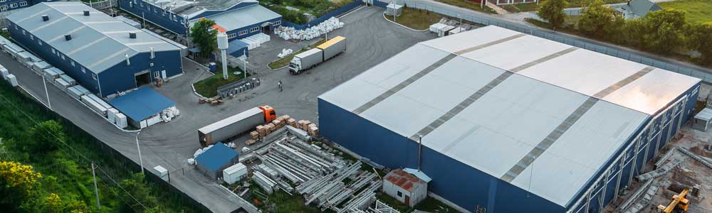 Aerial shot of factory building with metal roof, scrap metal outside and trucks arriving and leaving