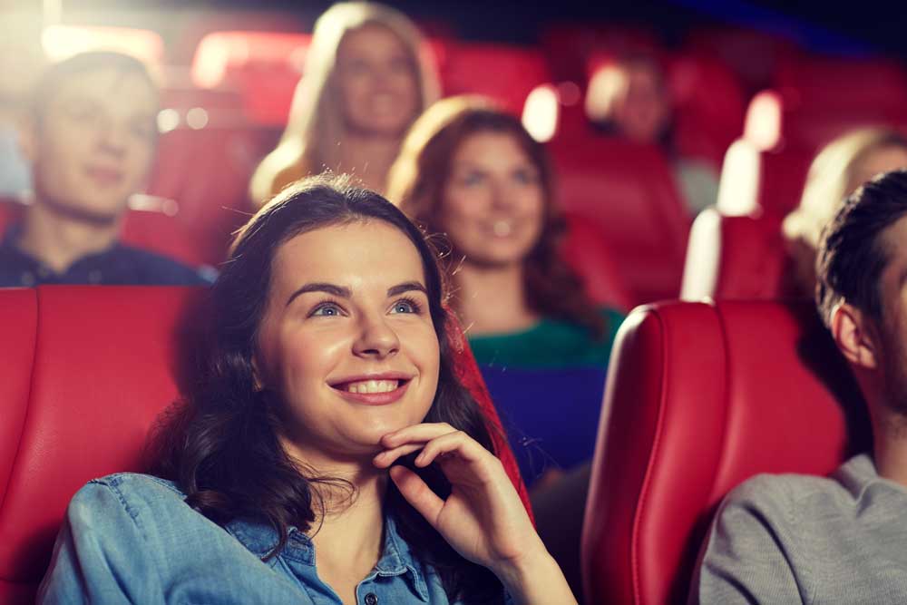 Girl smiles up at movie theater screen with other smiling people behind her